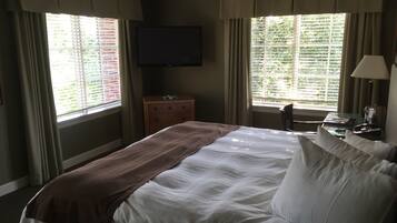A hotel room with a bed, a TV, a dresser, and a window with blinds.