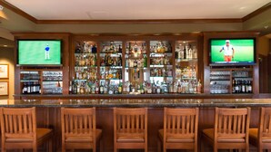 A bar area with multiple TVs displaying golf, a variety of liquor bottles, and wooden bar stools. - The Glen Club (Glenview)