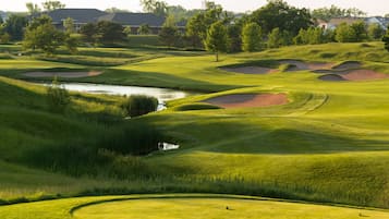 A golf course with sand bunkers, a pond, and houses in the background.
