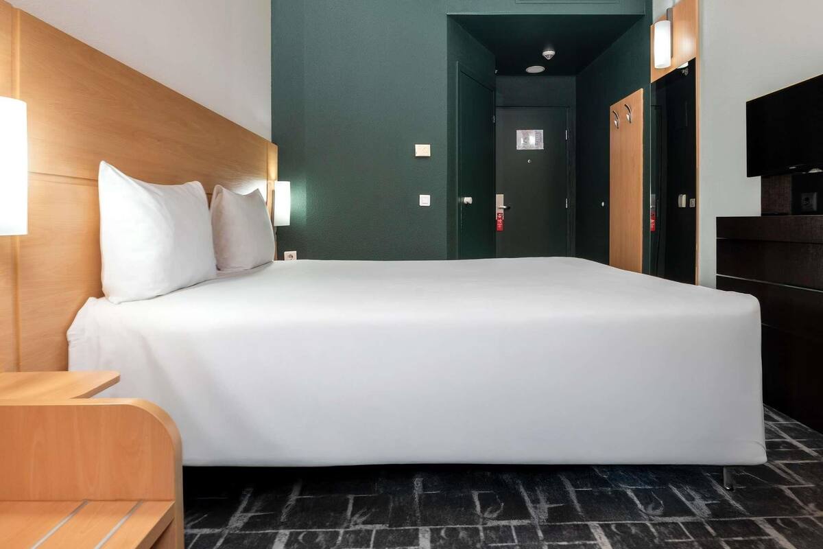 Habitación de hotel con una cama grande, cabecera de madera, mesita de noche, televisor y armario.