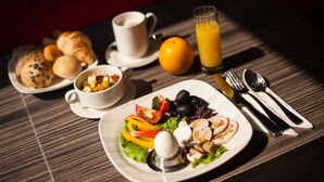 Una mesa de desayuno con croissants, ensalada de frutas, un plato con huevos, verduras y champiñones, un vaso de jugo de naranja y una taza de café.