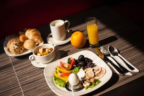 A breakfast setting with croissants, a fruit salad, a plate with eggs, vegetables, and mushrooms, a glass of orange juice, and a cup of coffee. - ibis Astana (Astana)
