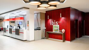 A reception desk with a red wall and a framed 'ibis' sign, a modern ceiling with pendant lights, and a clean, tiled floor. - ibis Astana (Astana)
