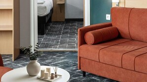 A modern hotel room with a large orange sofa, a white round table with a vase and candles, and a patterned floor. - ibis Astana (Astana)