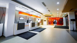 A modern hotel reception area with a reception desk, a digital screen, and a red-themed restaurant in the background. - ibis Astana (Astana)