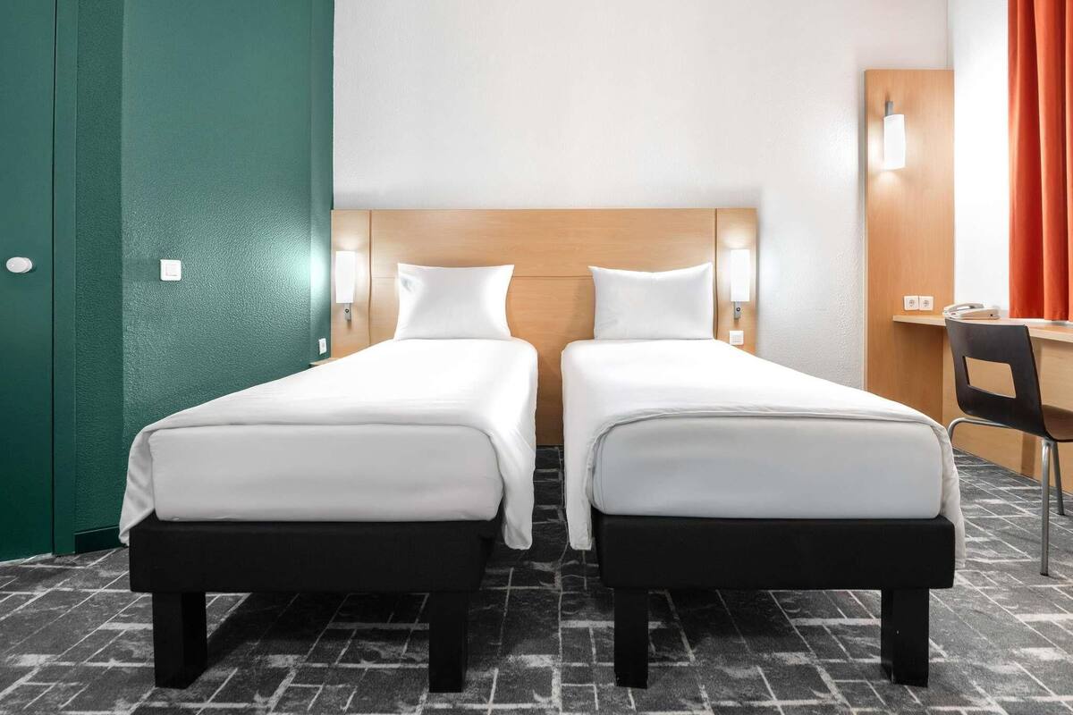 Una habitación de hotel con dos camas, un escritorio, una silla y una puerta verde.