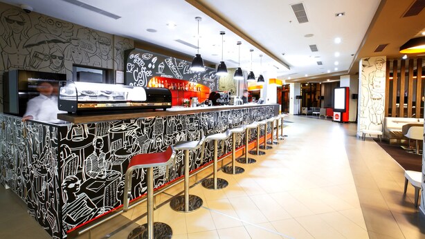 Zona de bar moderna con una barra larga, varios taburetes y una pared con ilustraciones en blanco y negro.