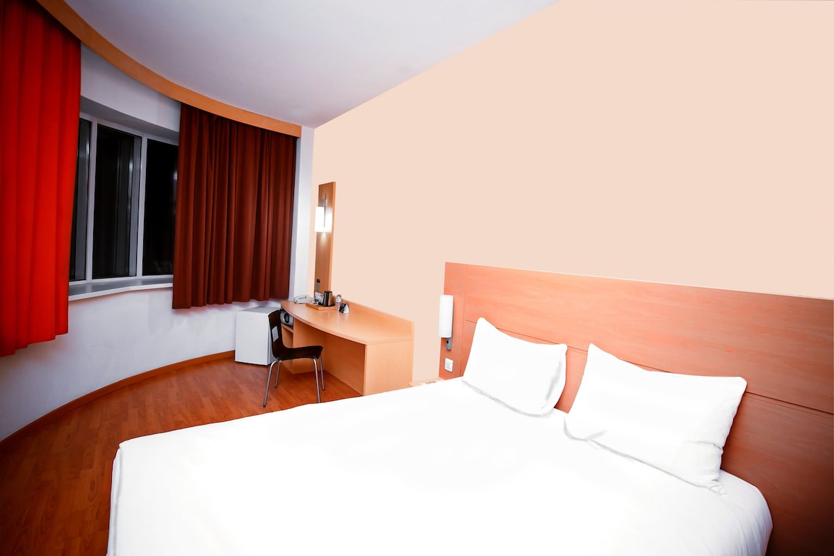 A hotel room with a bed, a desk, a chair, and a window with curtains.