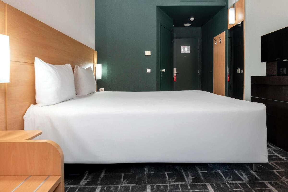 Habitación de hotel con una cama grande, cabecera de madera, mesita de noche, televisor y armario.