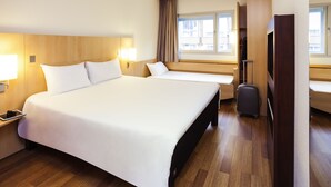 Habitación de hotel con una cama grande, un escritorio con lámpara, una maleta y un televisor.