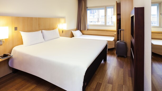 Habitación de hotel con una cama grande, un escritorio con lámpara, una maleta y un televisor.