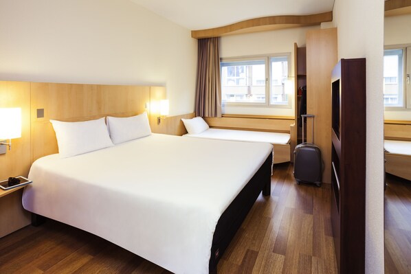 A hotel room with a large bed, a desk with a lamp, a suitcase, and a TV. - ibis Astana (Astana)