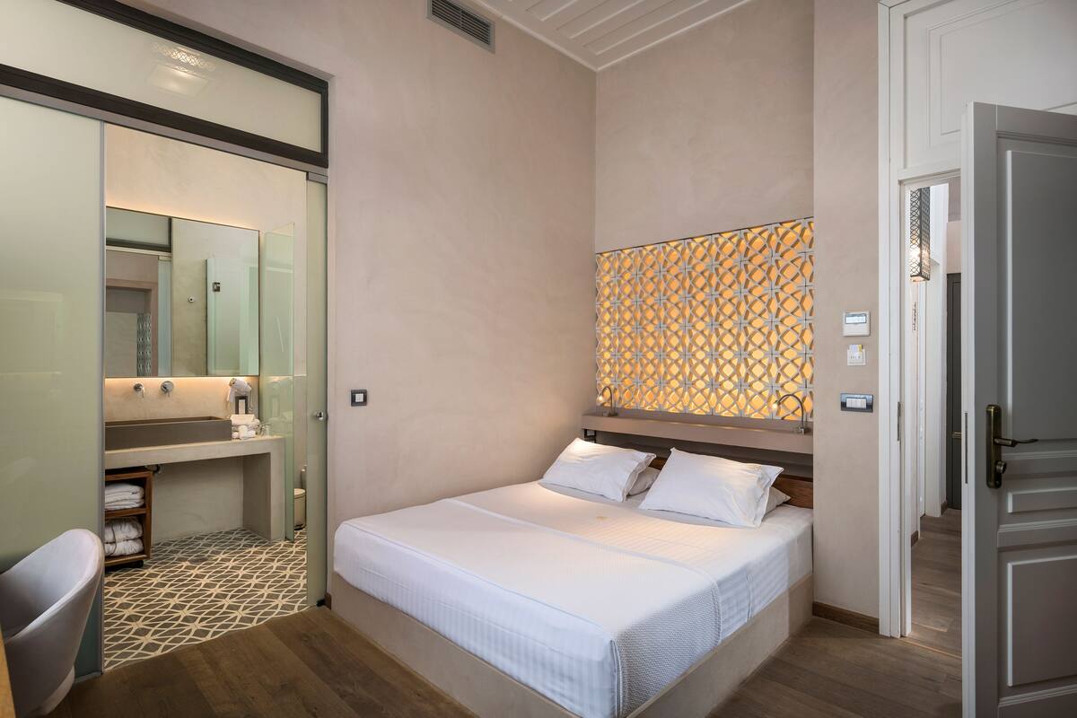A bedroom with a bed, a bedside table, a mirror, a sink, and a shower area.