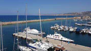 A marina with various boats docked, a small building with a sign, and a clear view of the sea and distant land.