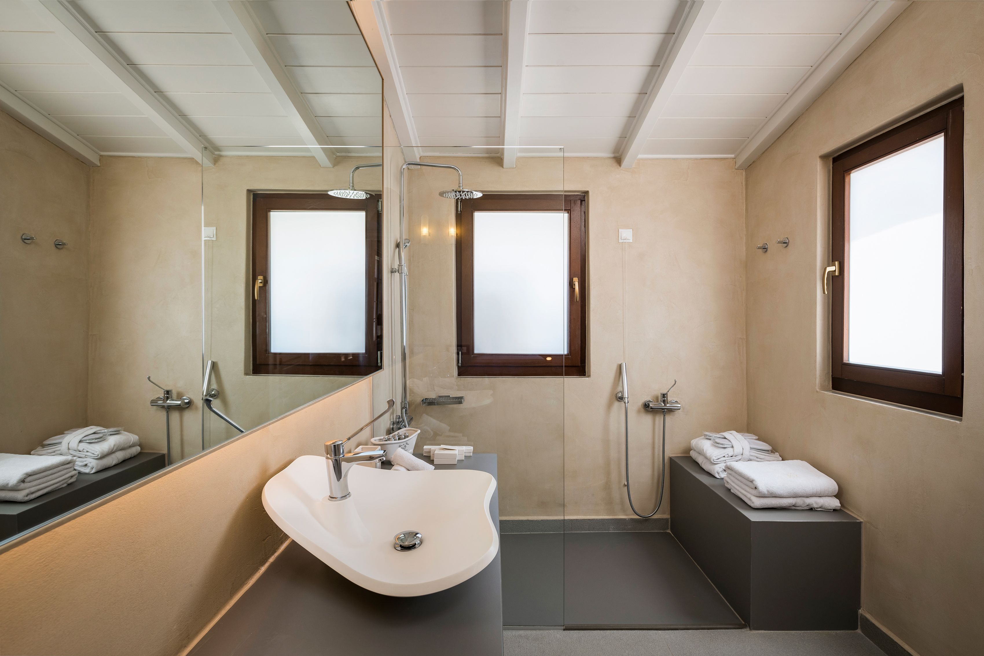 A modern bathroom with a large mirror, a sink, a shower, and two windows.