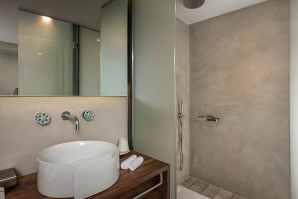 A modern bathroom with a large white sink, a mirror, and a shower area.