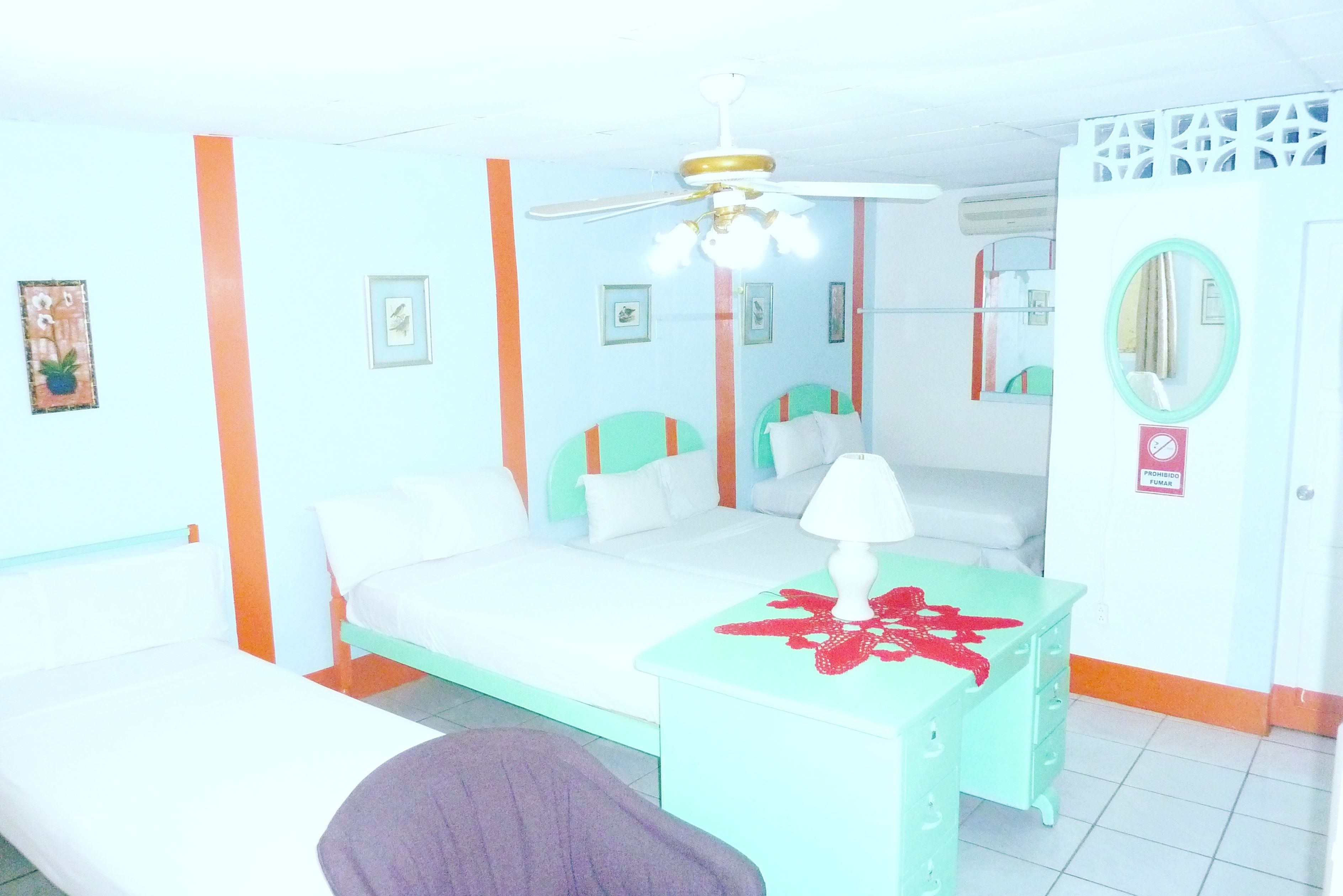 A room with a bed, a desk with a lamp, a mirror, and a ceiling fan.