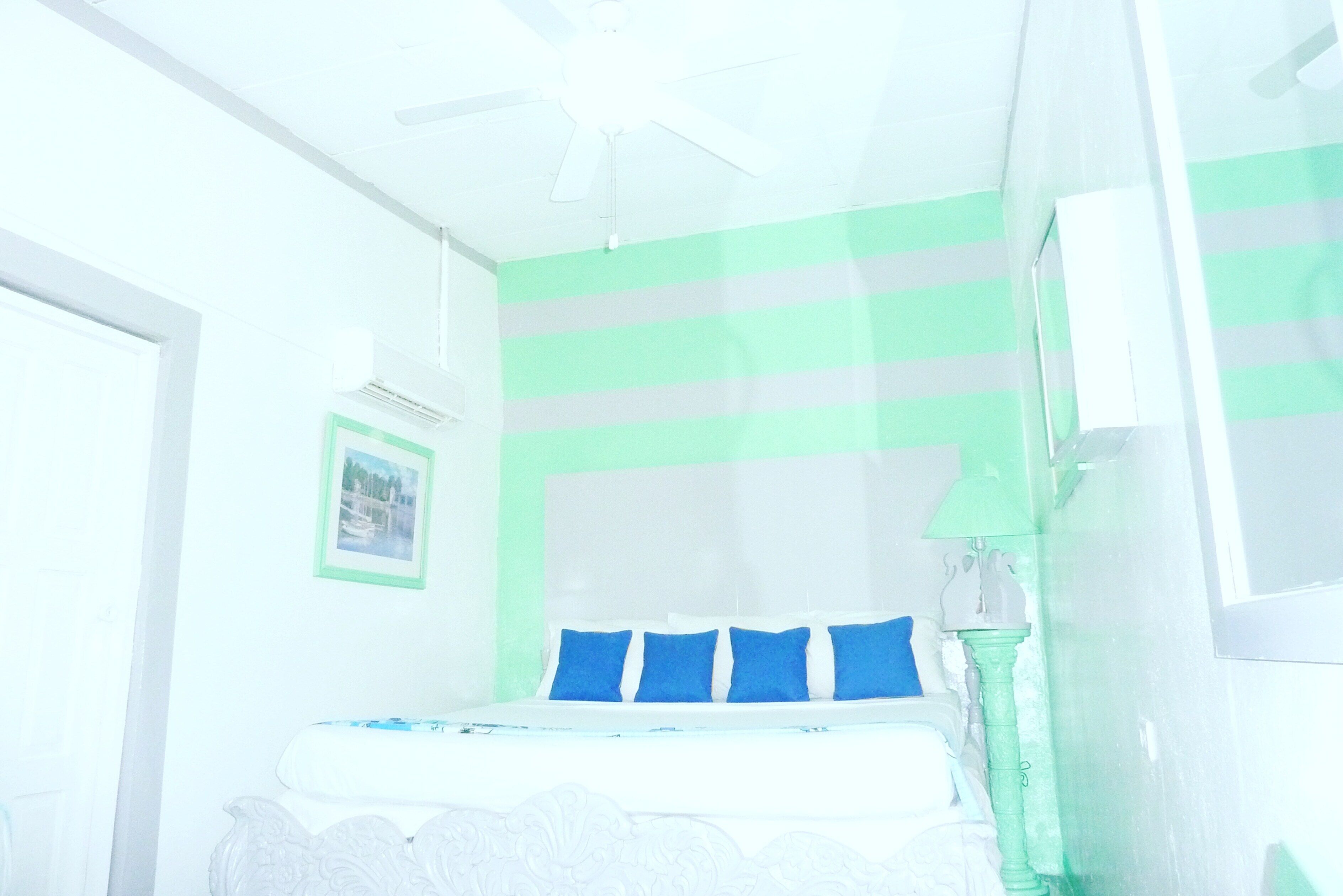 Una camera da letto con un letto, una ventola a soffitto, un quadro al muro e una finestra.