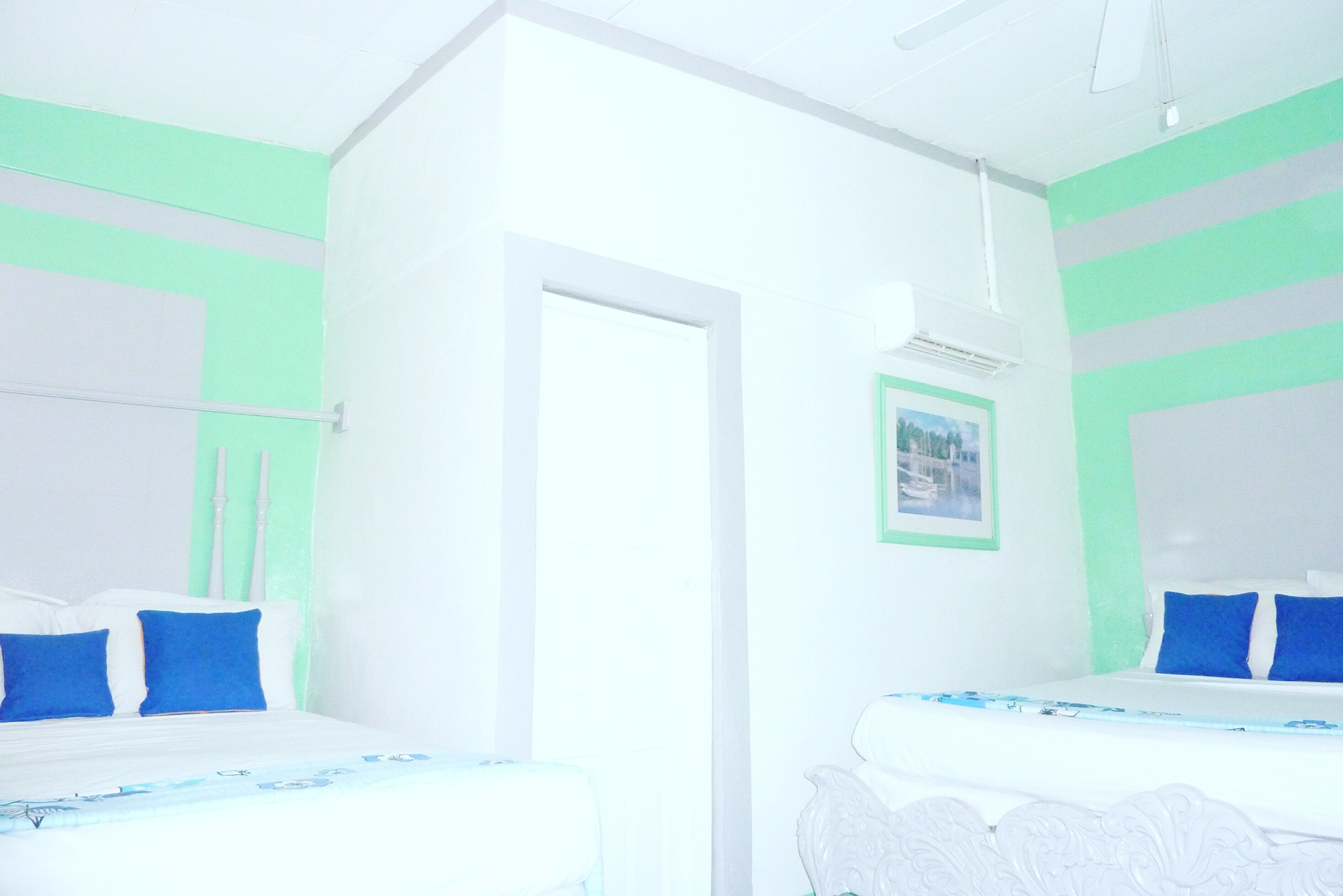 A hotel room with two beds, a door, and a framed picture on the wall.