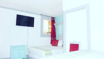 Une chambre à coucher avec un lit, une petite table de chevet, un téléviseur fixé au mur et une fenêtre avec des rideaux.