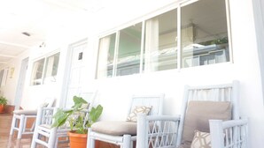 A row of white wicker chairs with cushions, a potted plant, and a large window with curtains. - Hotel Ivania's (Masaya)