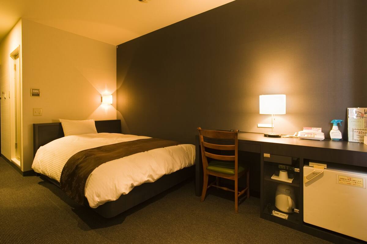 Une chambre d’hôtel équipée d’un lit, d’un bureau, d’une chaise et d’un petit réfrigérateur.