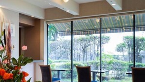 Een moderne hotellobby met een groot raam dat uitzicht geeft op een tuin. In het midden staan twee houten stoelen en een tafel.