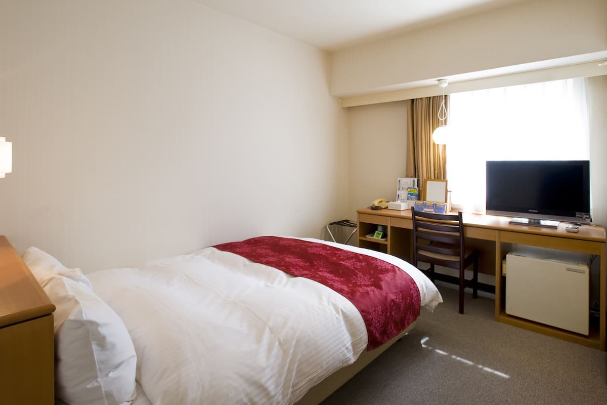 Une chambre d’hôtel équipée d’un lit, d’un bureau, d’une chaise, d’une télévision et d’un petit réfrigérateur.