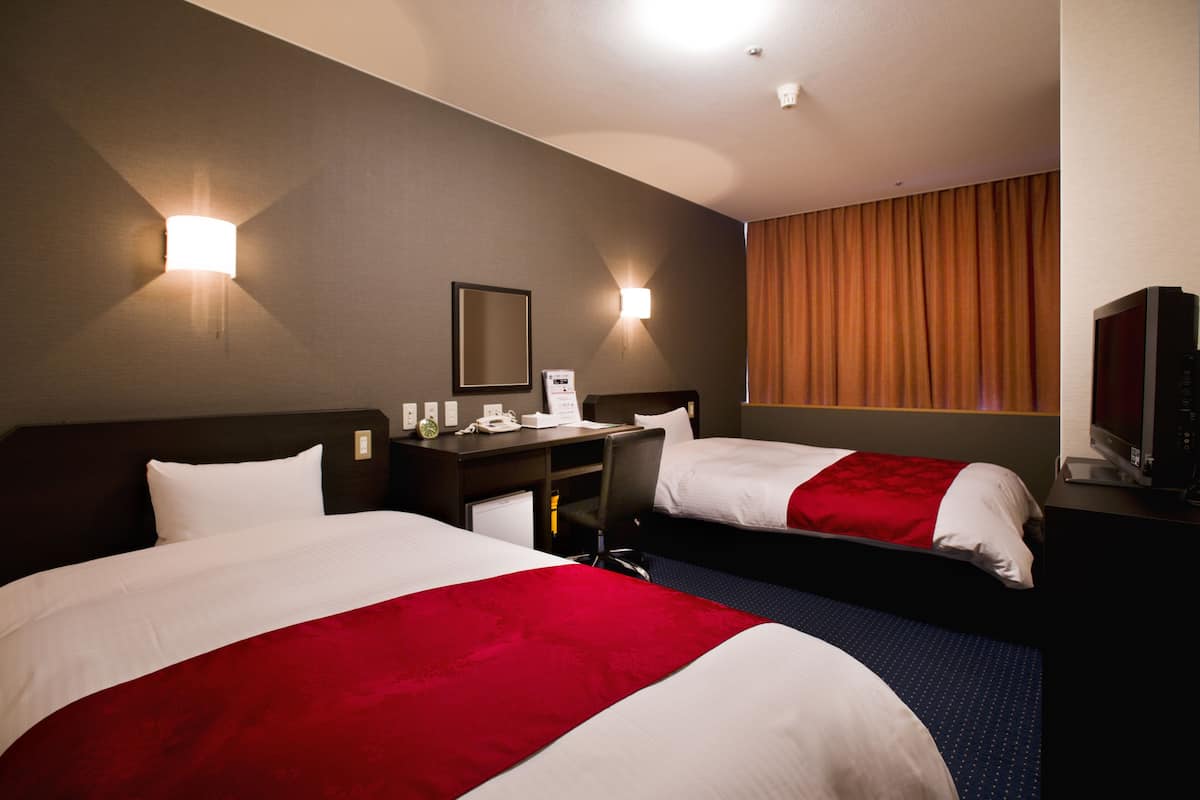 Une chambre d’hôtel avec deux lits, un bureau, une chaise, une tél évision et une fenêtre avec des rideaux.