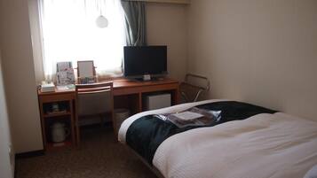 A hotel room with a bed, a desk with a computer, a chair, a small table with a coffee maker, and a window with curtains.