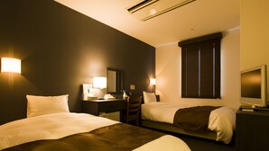Hotelkamer met twee bedden, een bureau, een stoel, een televisie en een raam met jaloezieën.