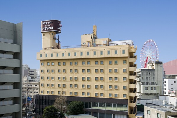 Un hotel de varios pisos con fachada moderna, un tanque de agua visible en el techo y una noria al fondo.
