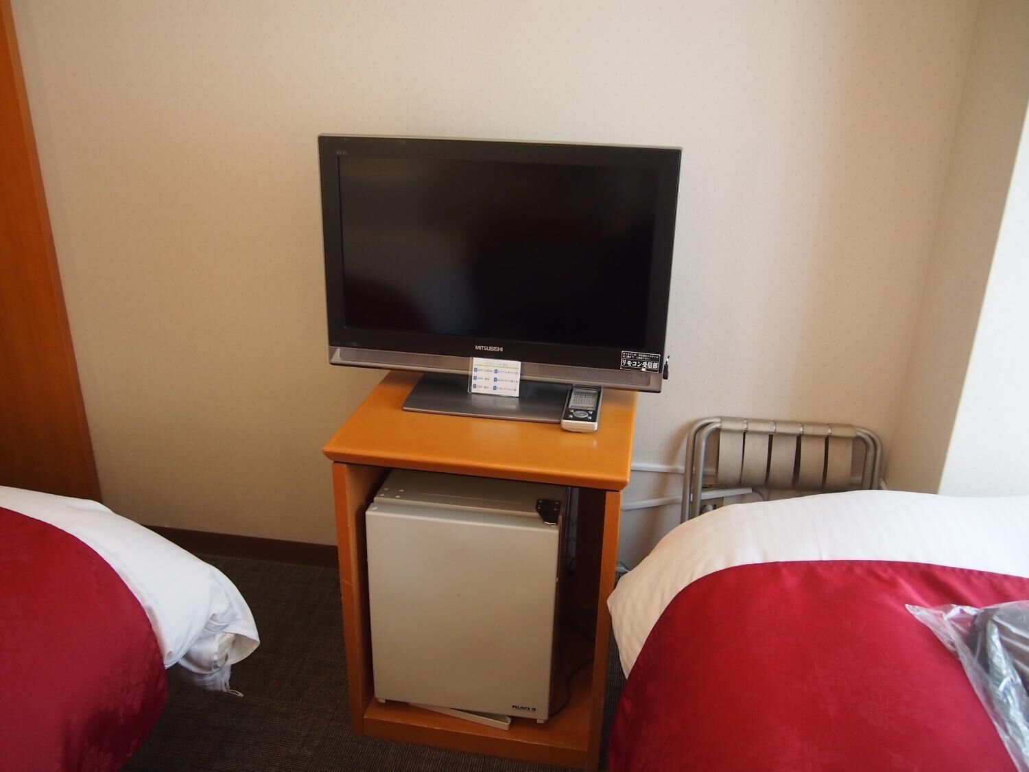 A hotel room with two beds, a television on a stand, and a small refrigerator.