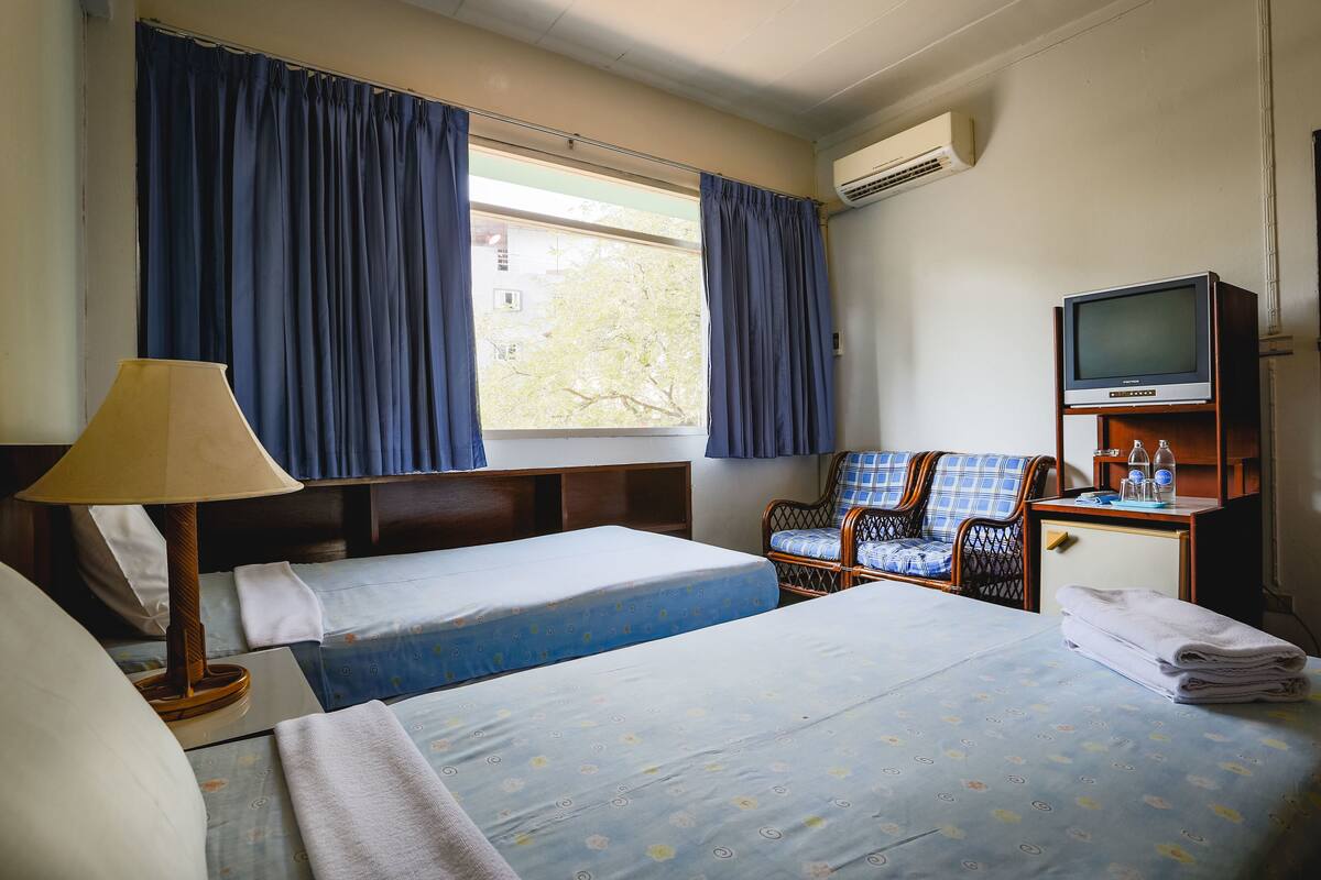A hotel room with two beds, a TV on a wooden stand, a chair, and a window with curtains.