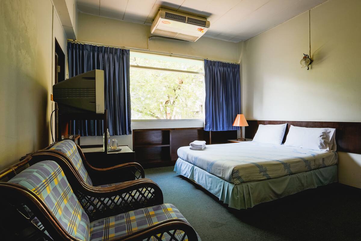A hotel room with a bed, a chair, a desk, and a window with curtains.