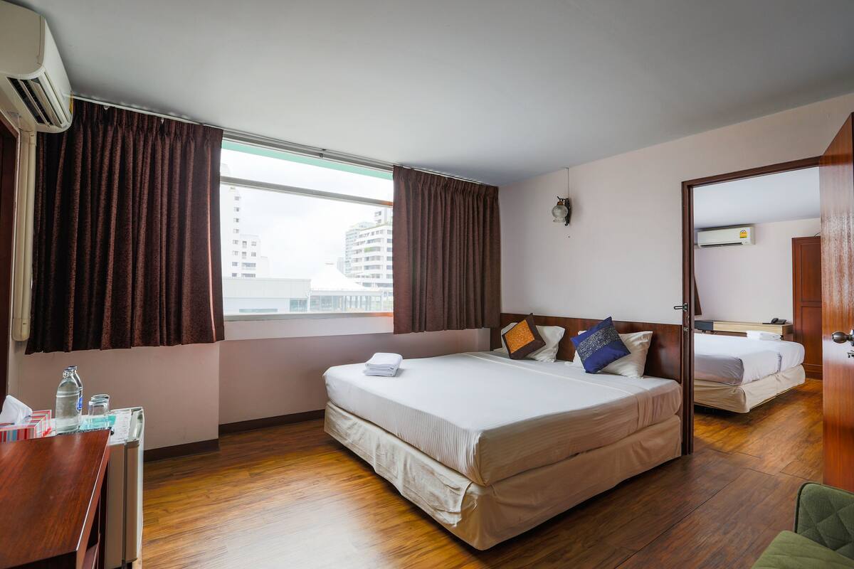 A hotel room with a large bed, a smaller bed, a desk with a chair, and a window with curtains.