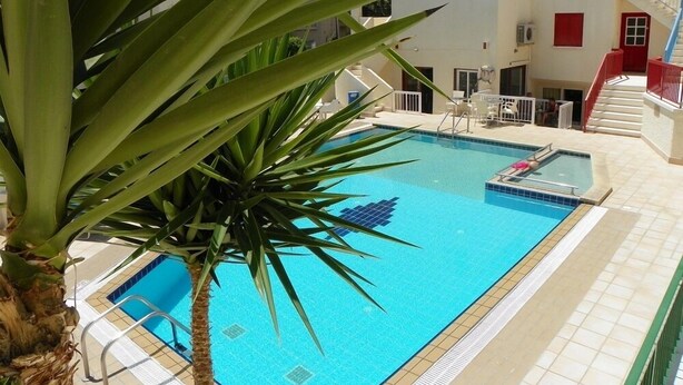 Una piscina con borde de baldosas, rodeada por un edificio de fachada blanca y detalles azules.