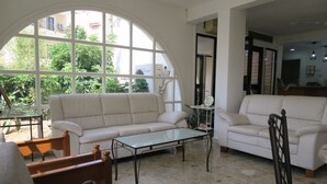 Un salón amplio con un gran ventanal arqueado, un sofá blanco, una mesa de centro de vidrio y una silla de madera.