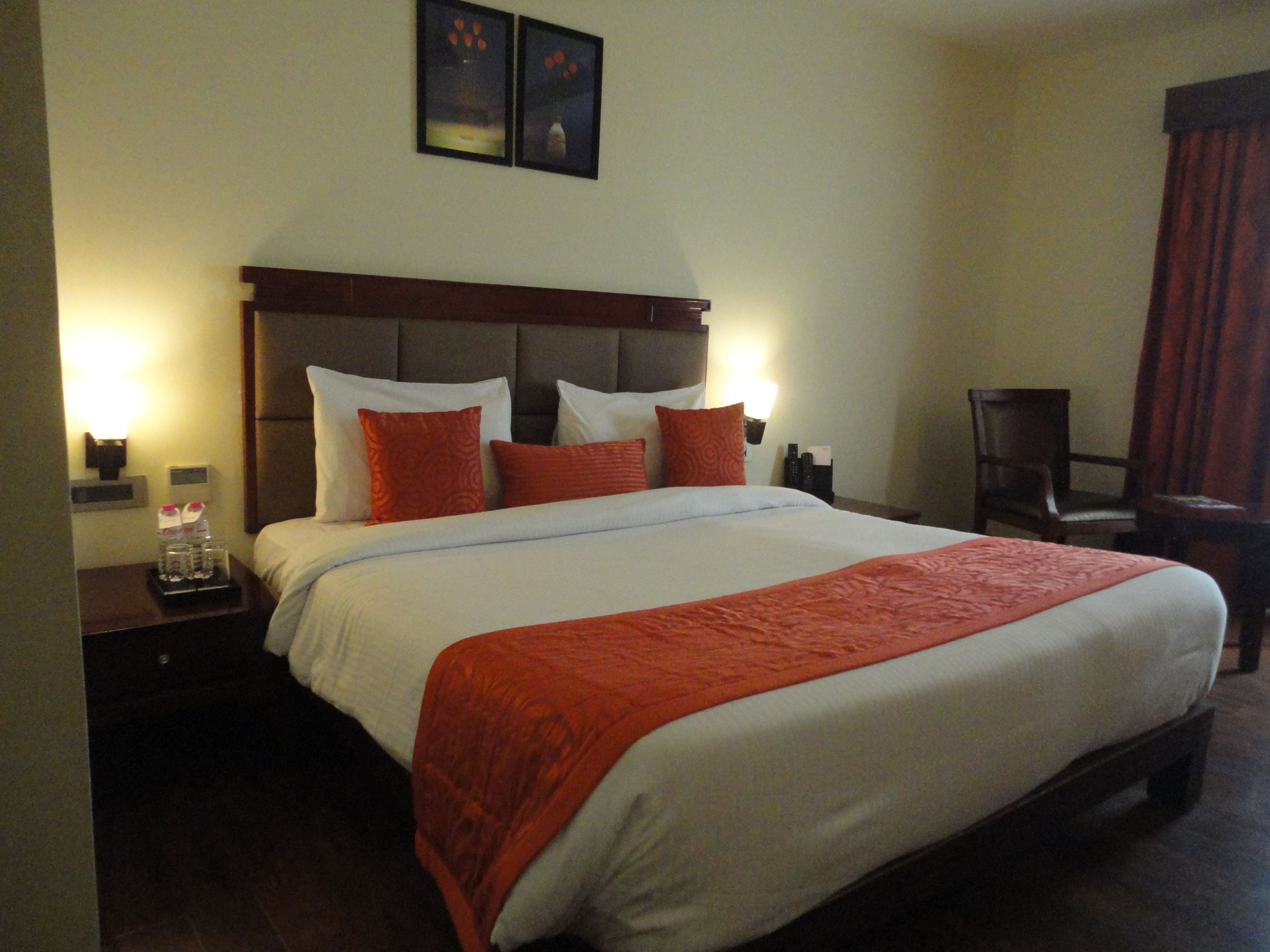 A hotel room with a large bed, two bedside tables, a nightstand, a chair, and a wall-mounted lamp.