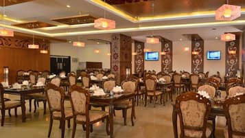Un amplio salón de banquetes con varias mesas y sillas, decoraciones ornamentales en las paredes y luces en el techo.