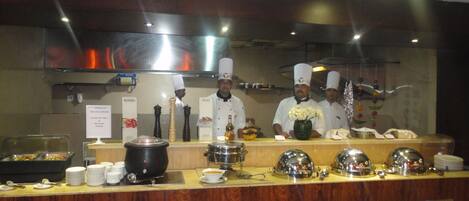 A buffet setup with chefs in uniform, a variety of dishes, and kitchen equipment.