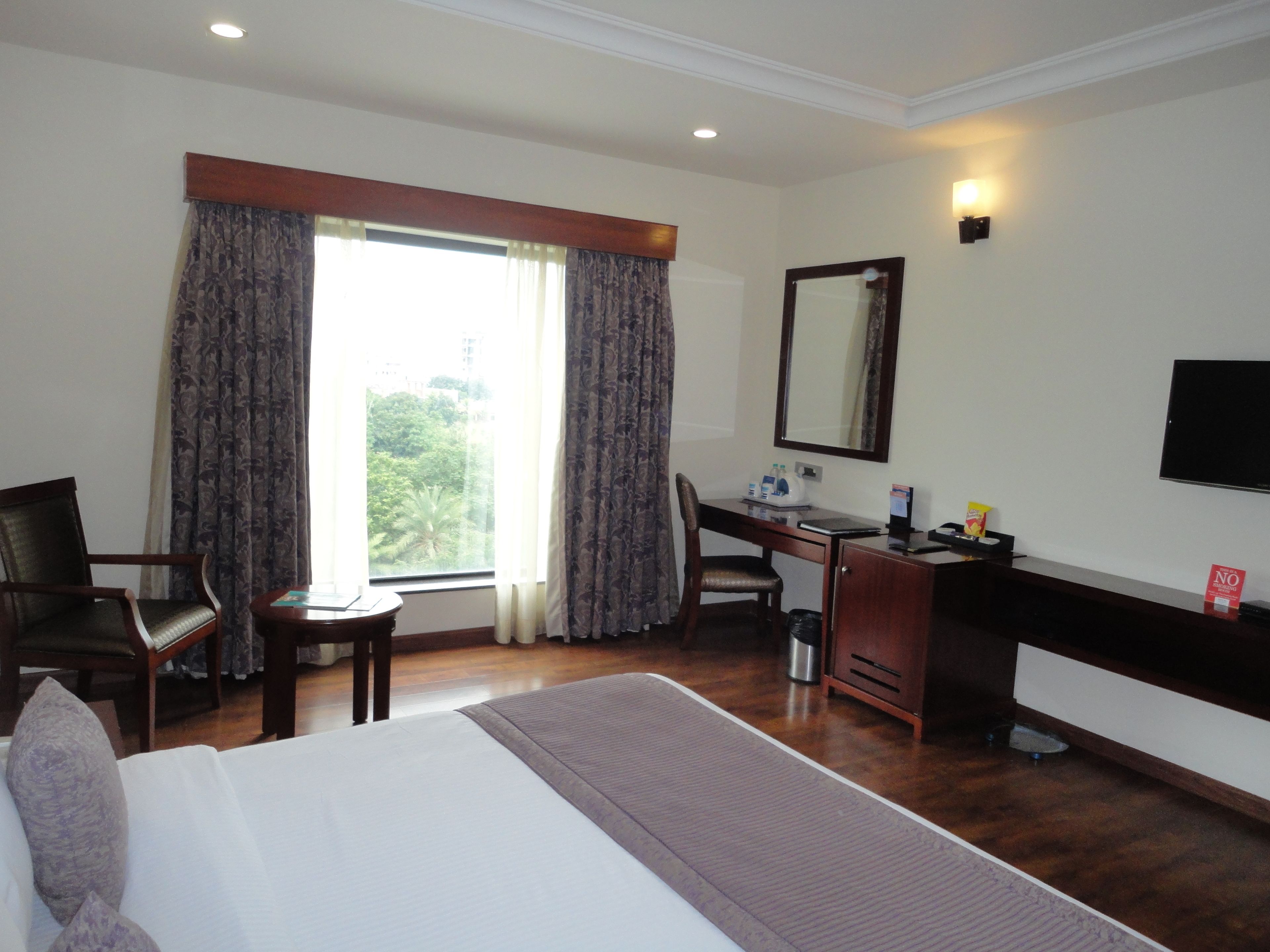 A hotel room with a bed, a desk, a chair, a TV, and a window with curtains.