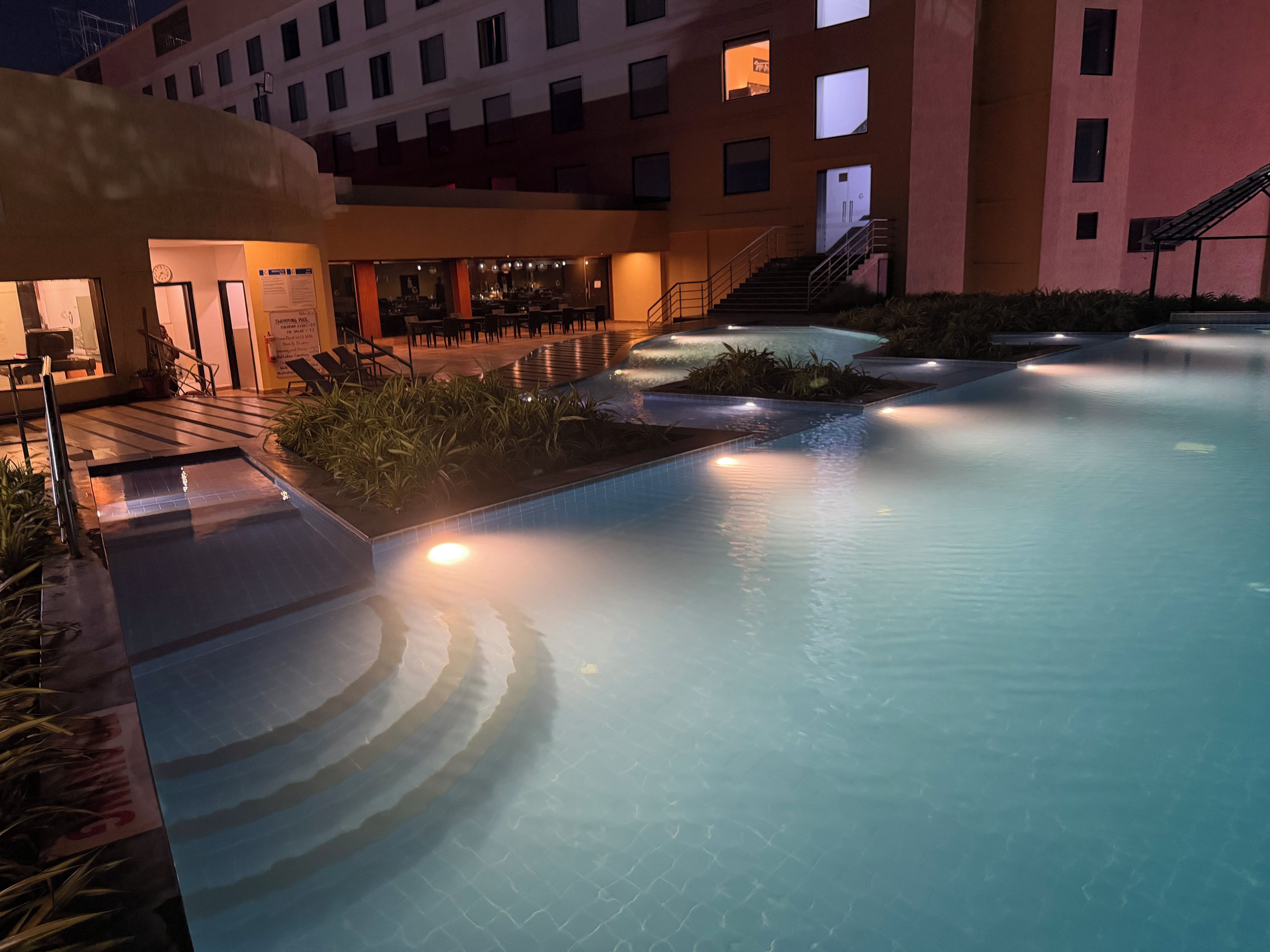 A swimming pool area with a sunken section, surrounded by a building with multiple windows and a staircase.