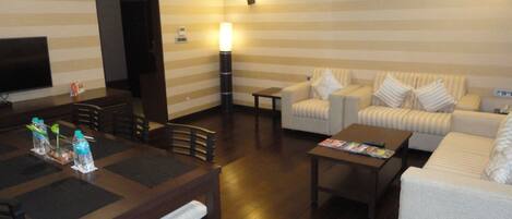 Habitación de hotel con comedor, sofá, televisor y lámpara.