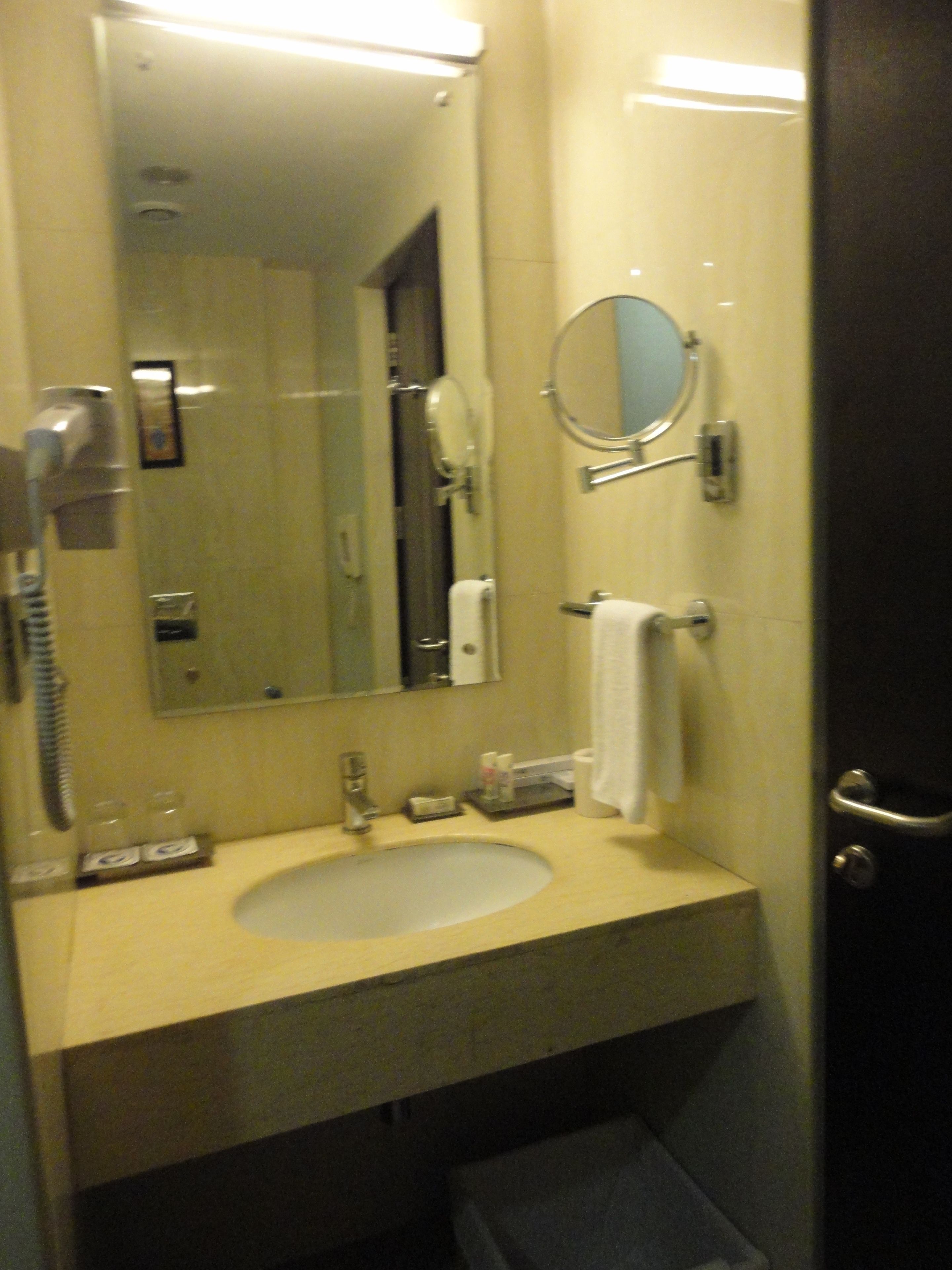 Une salle de bain d’hôtel équipée d’un lavabo, d’un miroir, d’un porte-serviettes et d’un sèche-cheveux.