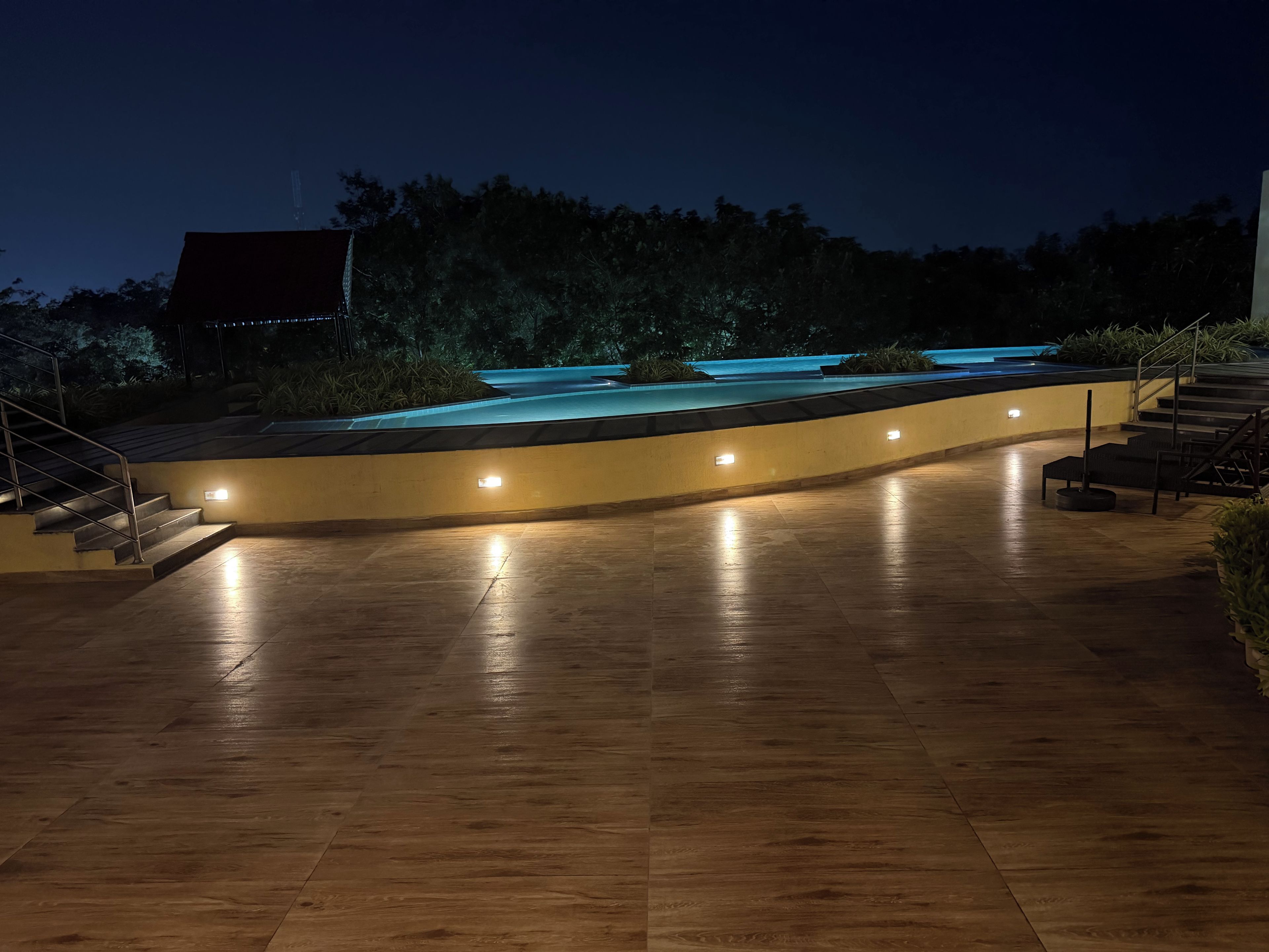 A nighttime outdoor area with a pool, steps, and a curved wall.