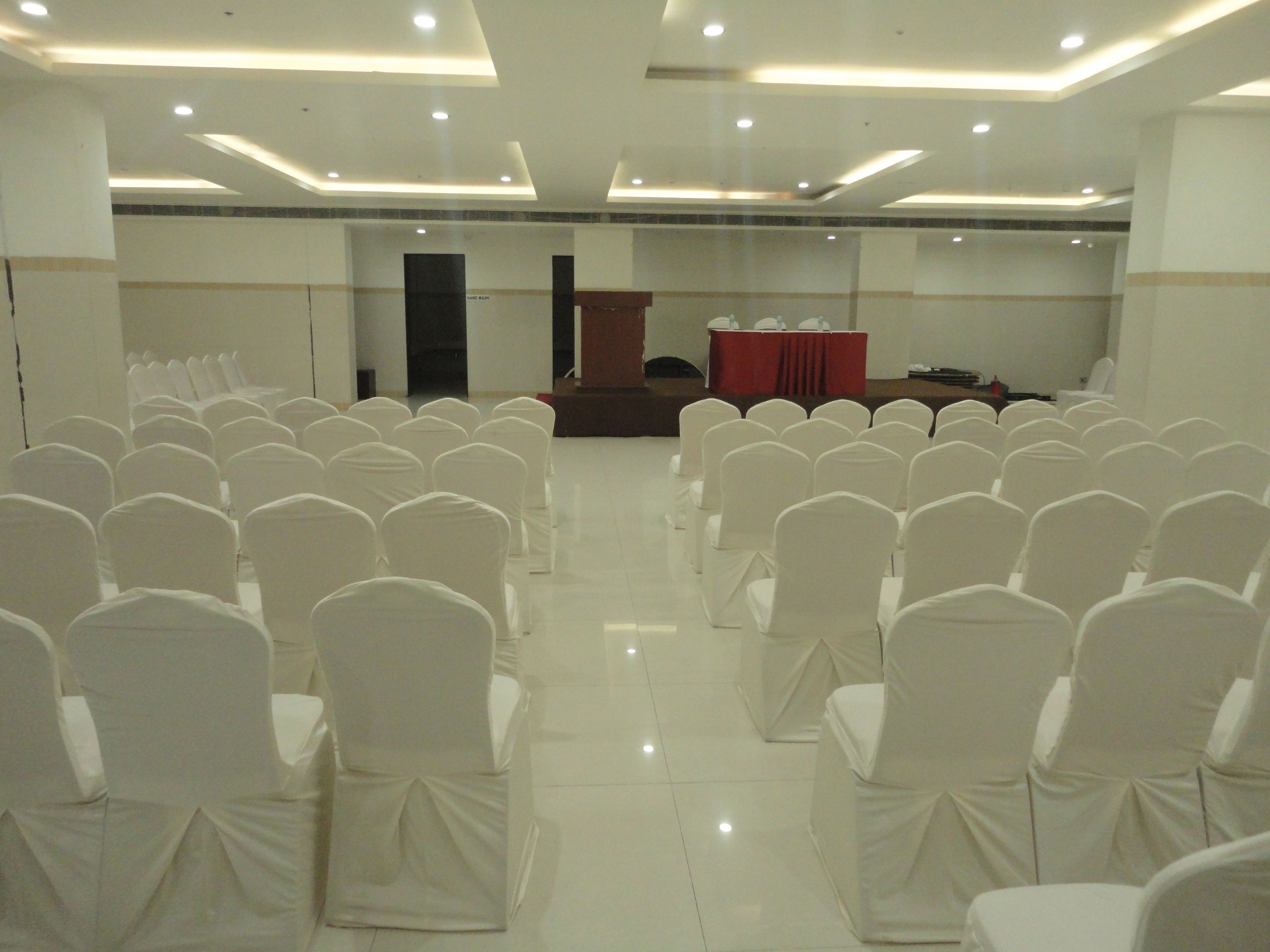 Une salle de conférence avec des rangées de chaises blanches et un pupitre à l’avant.
