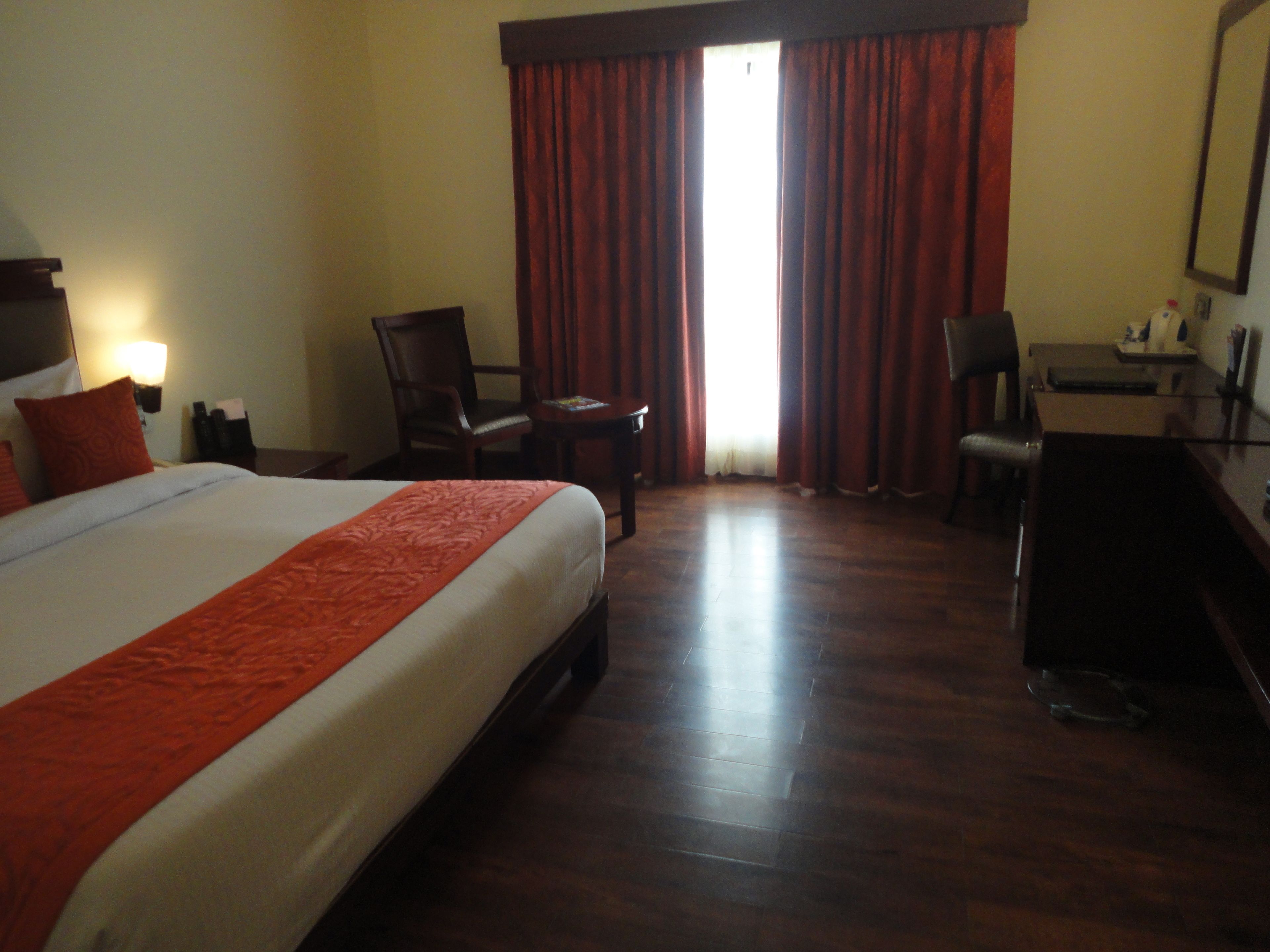 A hotel room with a large bed, two chairs, a desk, and a mirror.