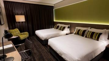 A hotel room with two beds, a desk, a chair, and a lamp.
