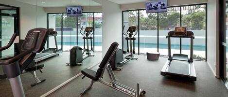 Un gimnasio moderno con máquinas de cardio, equipamiento de levantamiento de pesas y grandes ventanales con vistas al exterior.